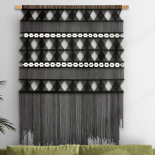 Large Sozarri monochrome macrame wall hanging on grey wall with plant and furniture